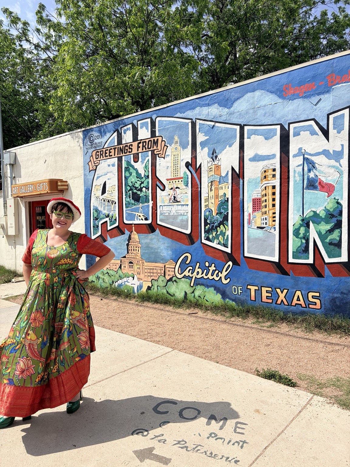 Sarah smiling in a colorful dress beside an Austin mural