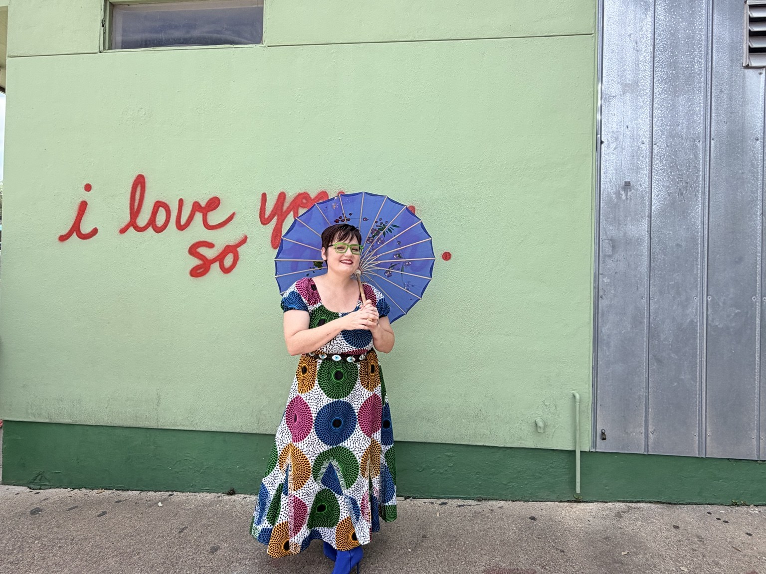 Sarah smiling beneath a blue umbrella in a bright patterned dress